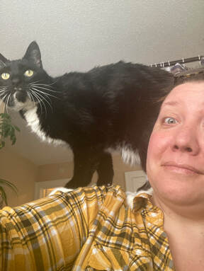 Image of Lindsay in a yellow plaid shirt, with her tuxedo cat Sgt. Pepper on her shoulder.